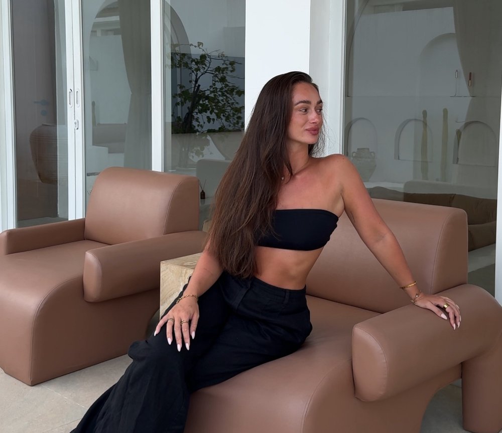 Laura Jasmin sitting on a tan sofa in front of white arched windows